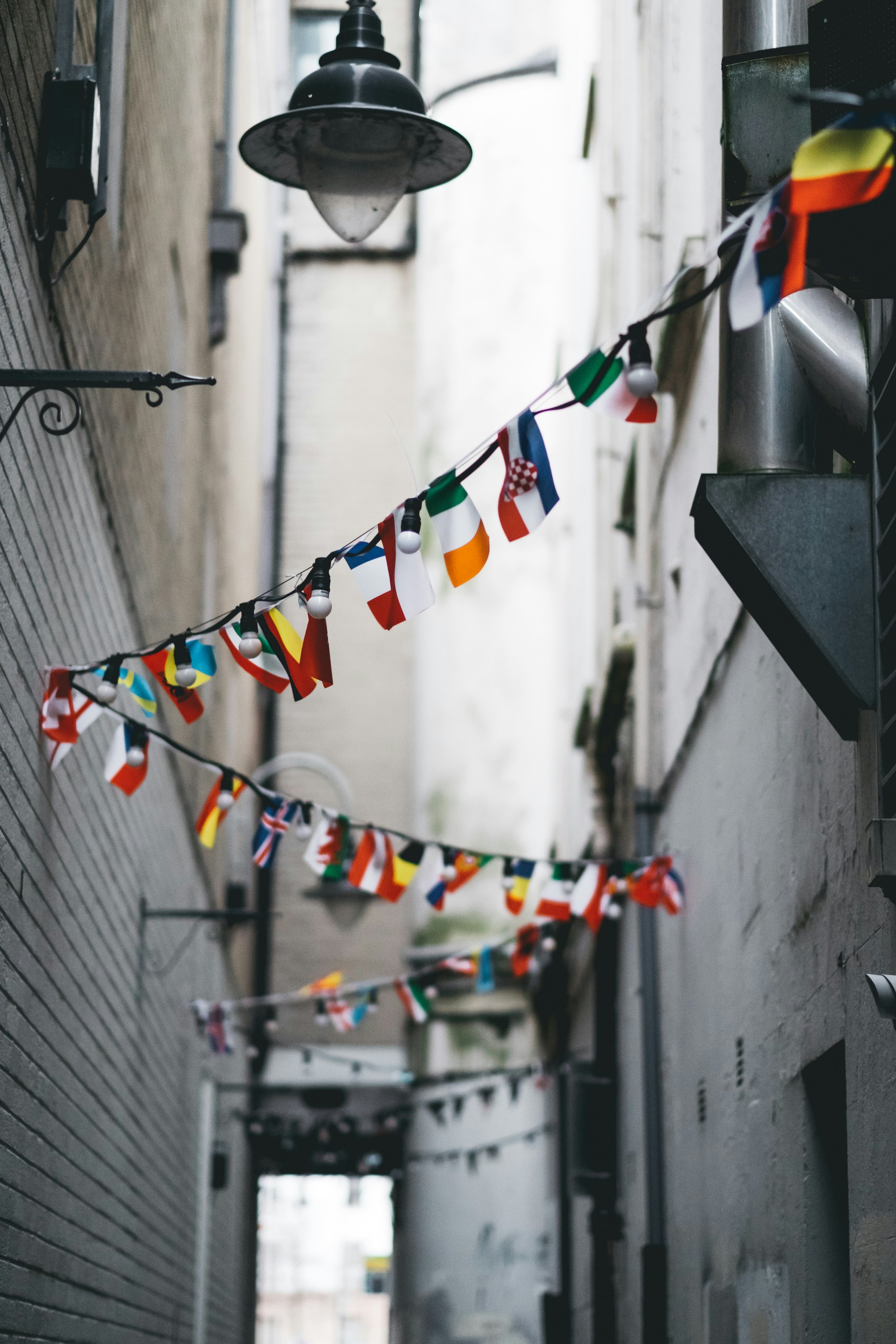 Strings of small international flags hang across a narrow alleyway, creating a festive and multicultural atmosphere.