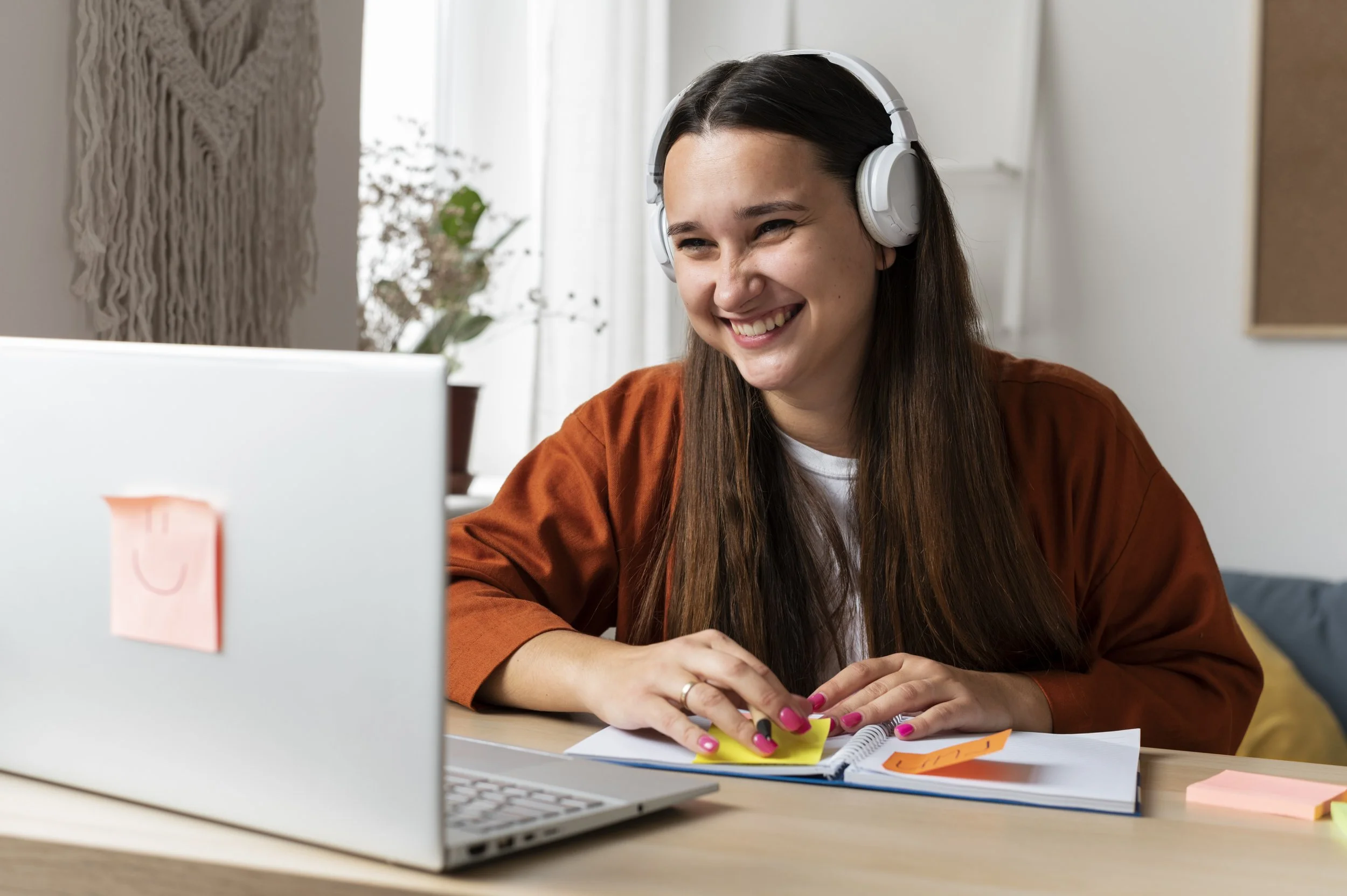 Smiling woman wearing headphones studying online with a laptop and notebook.