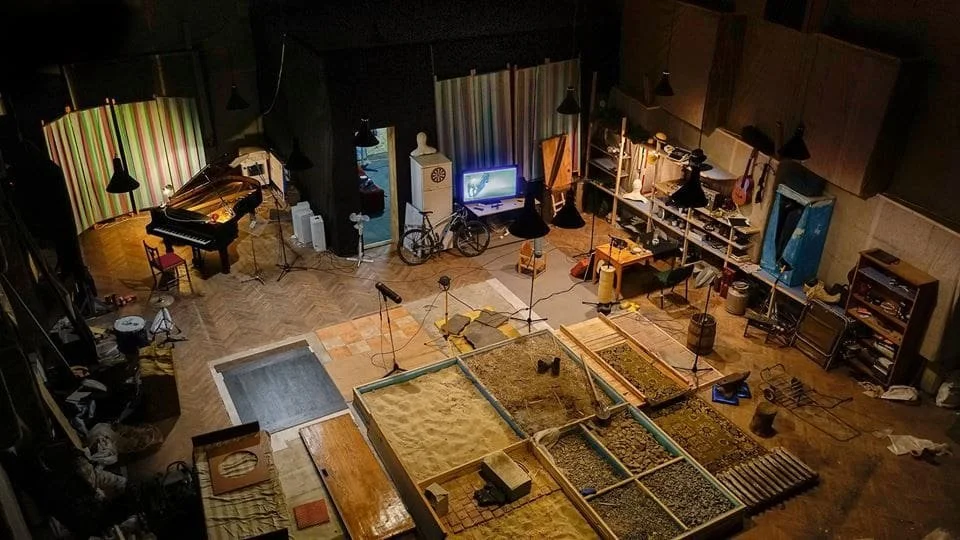 Artistic workshop with a piano, tools, sandpit, bicycle, and musical instruments.