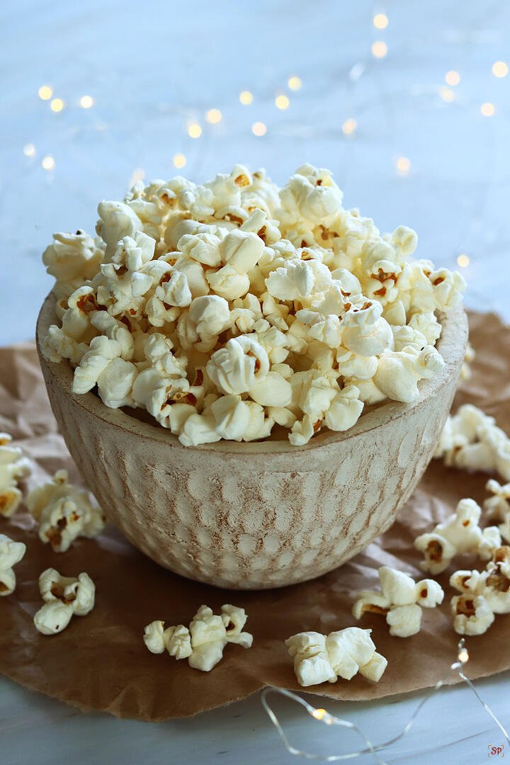 A rustic bowl overflowing with freshly popped popcorn, with scattered kernels around and soft string lights glowing in the background.