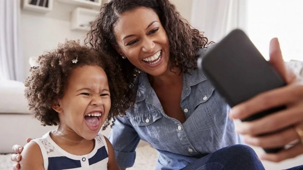 Mother and daughter laughing while taking a selfie together at home.