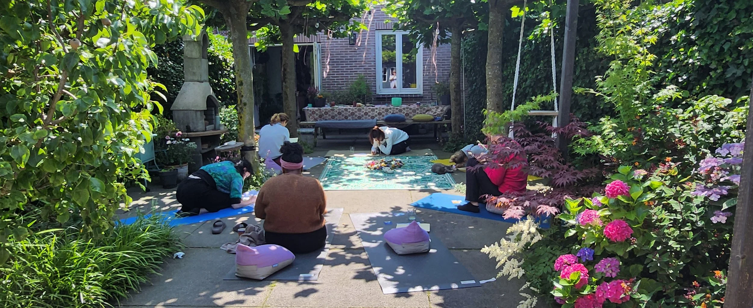 Group of people doing yoga outdoors in a garden with yoga mats and cushions