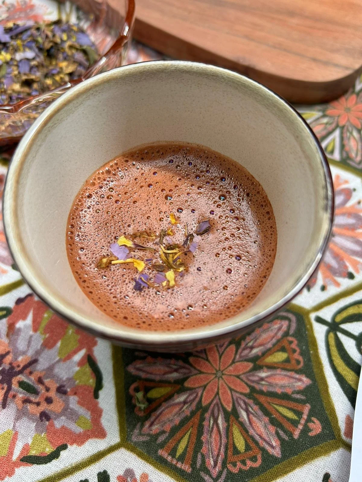 Cup of hot chocolate with foam and edible flowers on patterned tablecloth