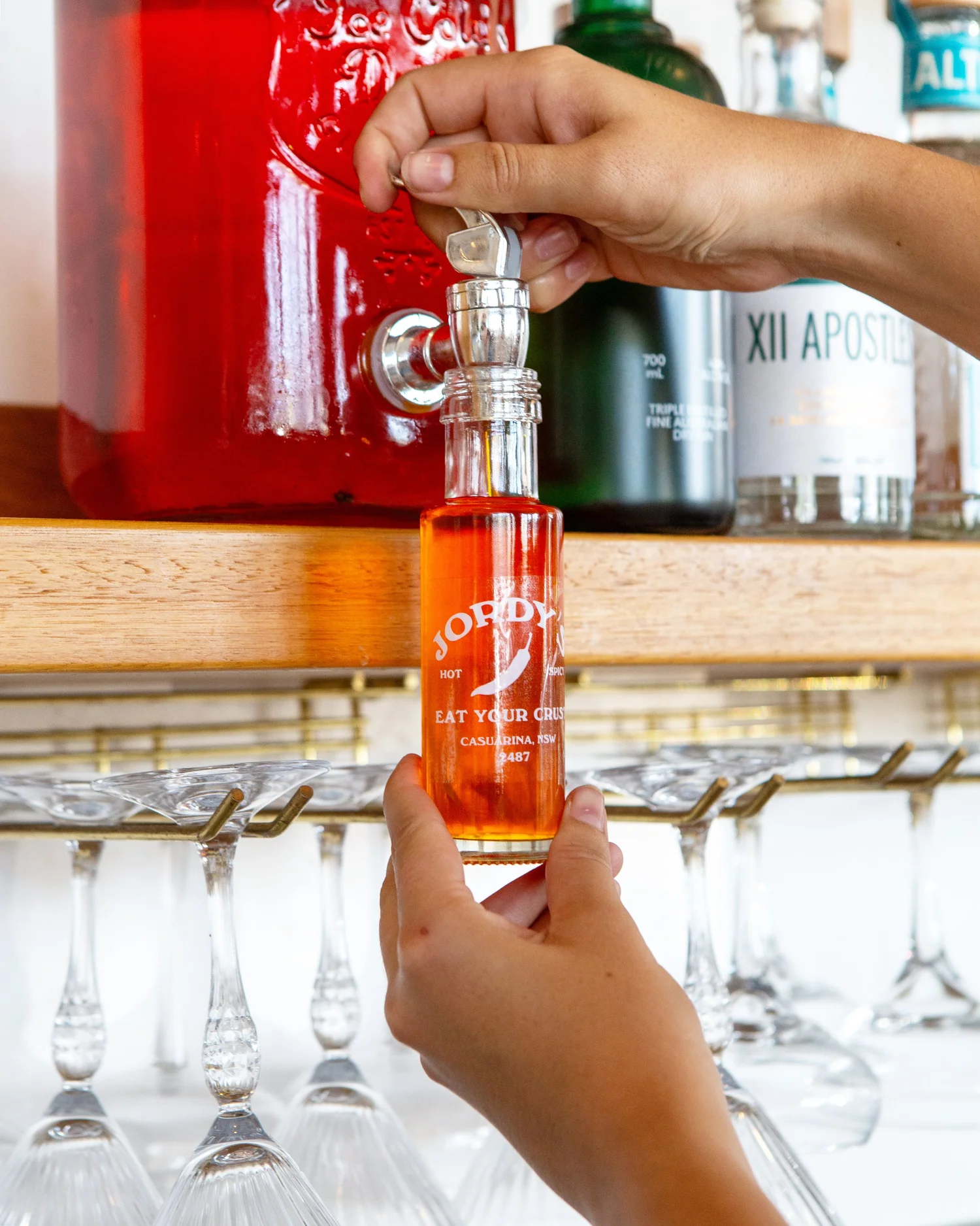 A 100ml bottle of Jordy's chilli oil being filled from a tap behind the bar at Jordy's Casuarina.