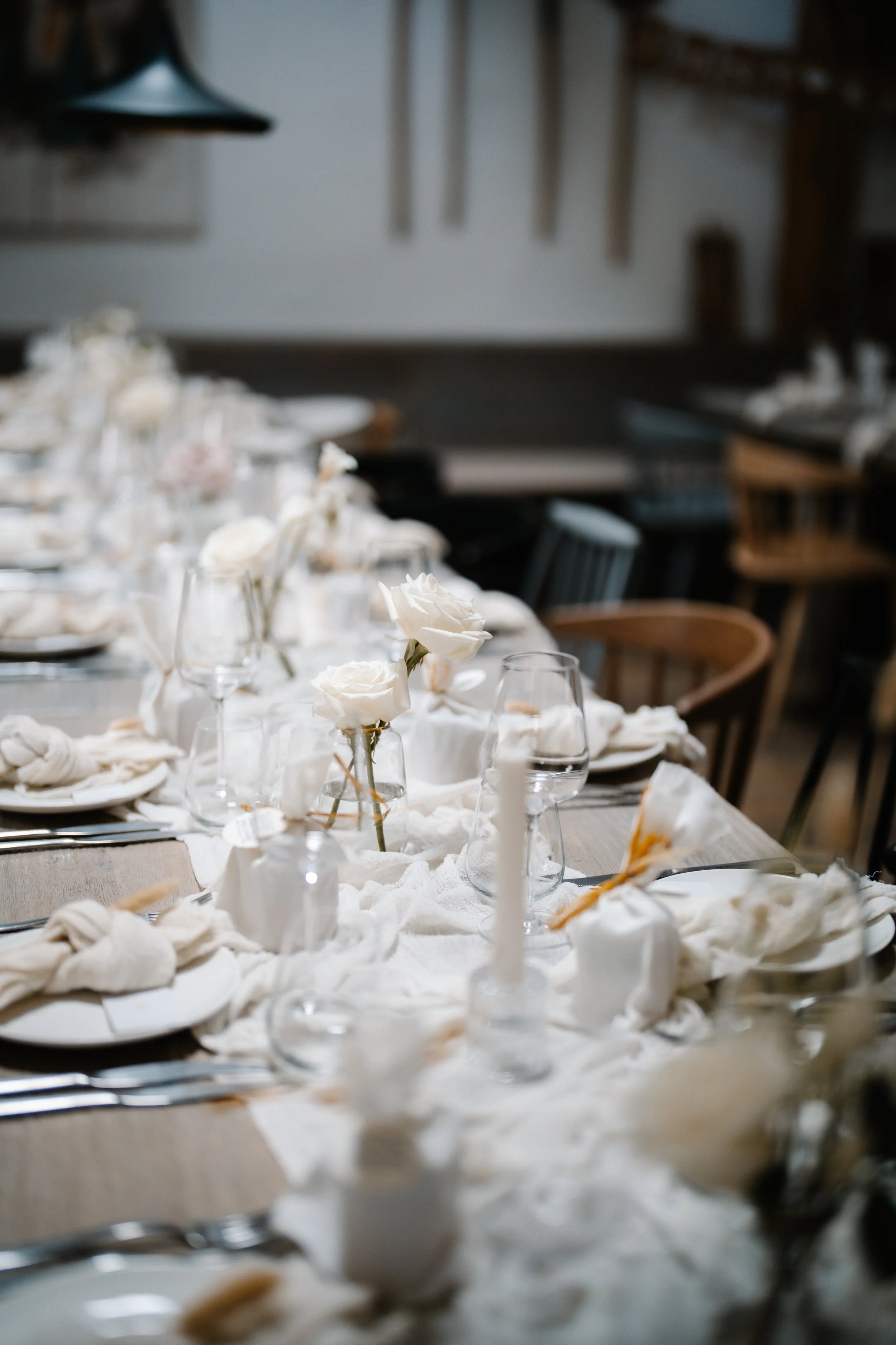 Ein gedeckter Tisch mit weißen Blumen in Gläsern, Kerzen und gedecktem Geschirr für eine elegante Veranstaltung.