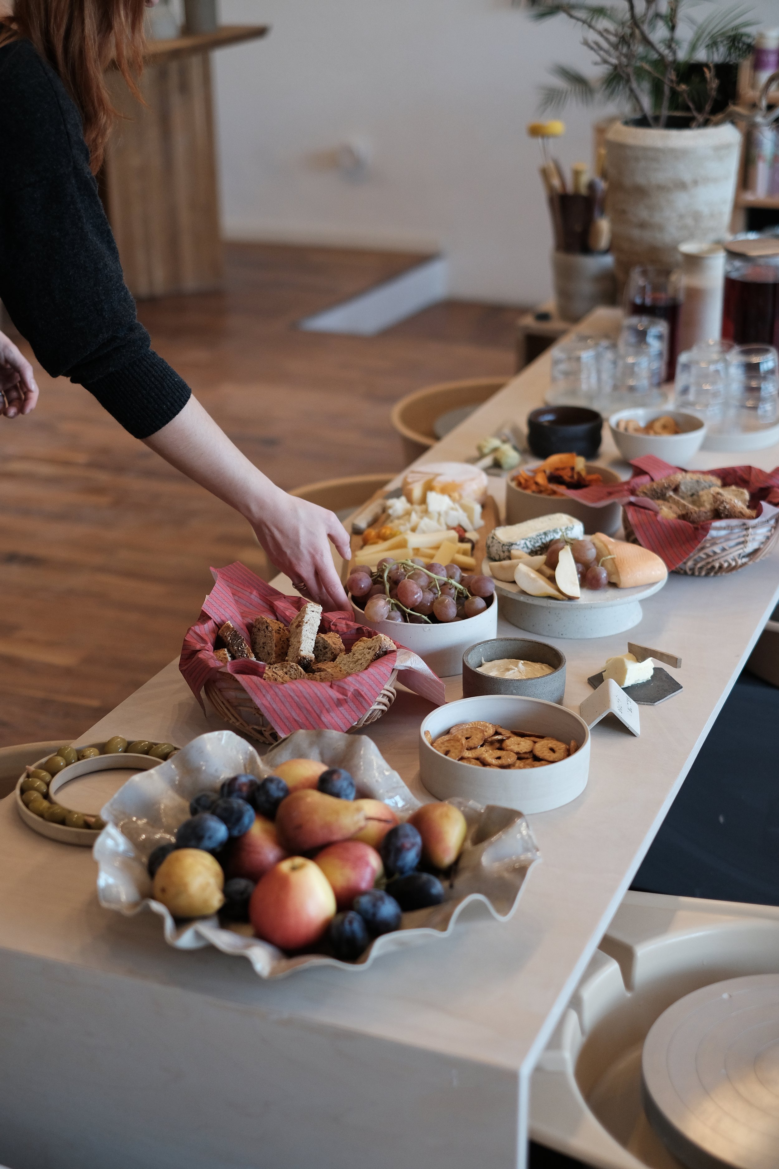 Bunte Früchte und Snacks auf einem Holztisch, im Hintergrund Keramikvasen mit Pflanzen und Gläser.