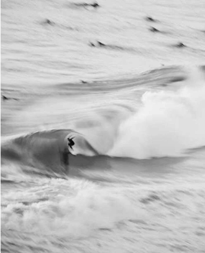 A person surfing on a wave in black and white.