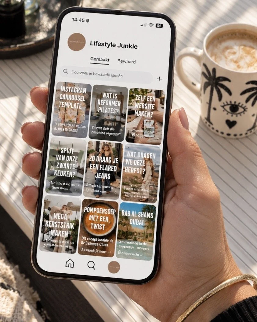Een hand houdt een iPhone vast met het Pinterest-profiel van Lifestyle Junkie op het scherm. Op tafel staat een cappuccino in een mok met palmboomprint.