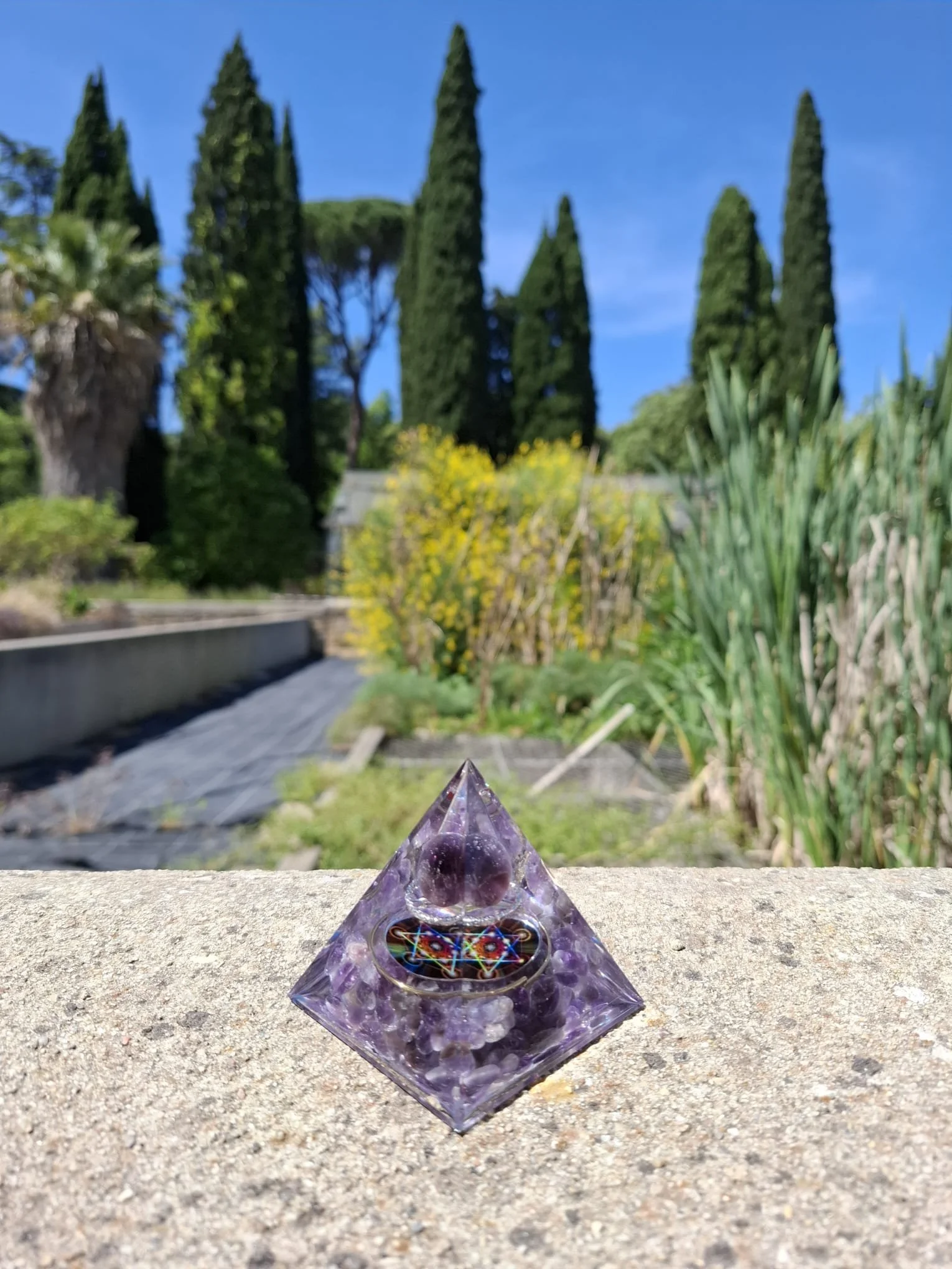 Orgonite artisanale d'améthyste posée au milieu d’un jardin, en harmonie avec la nature
