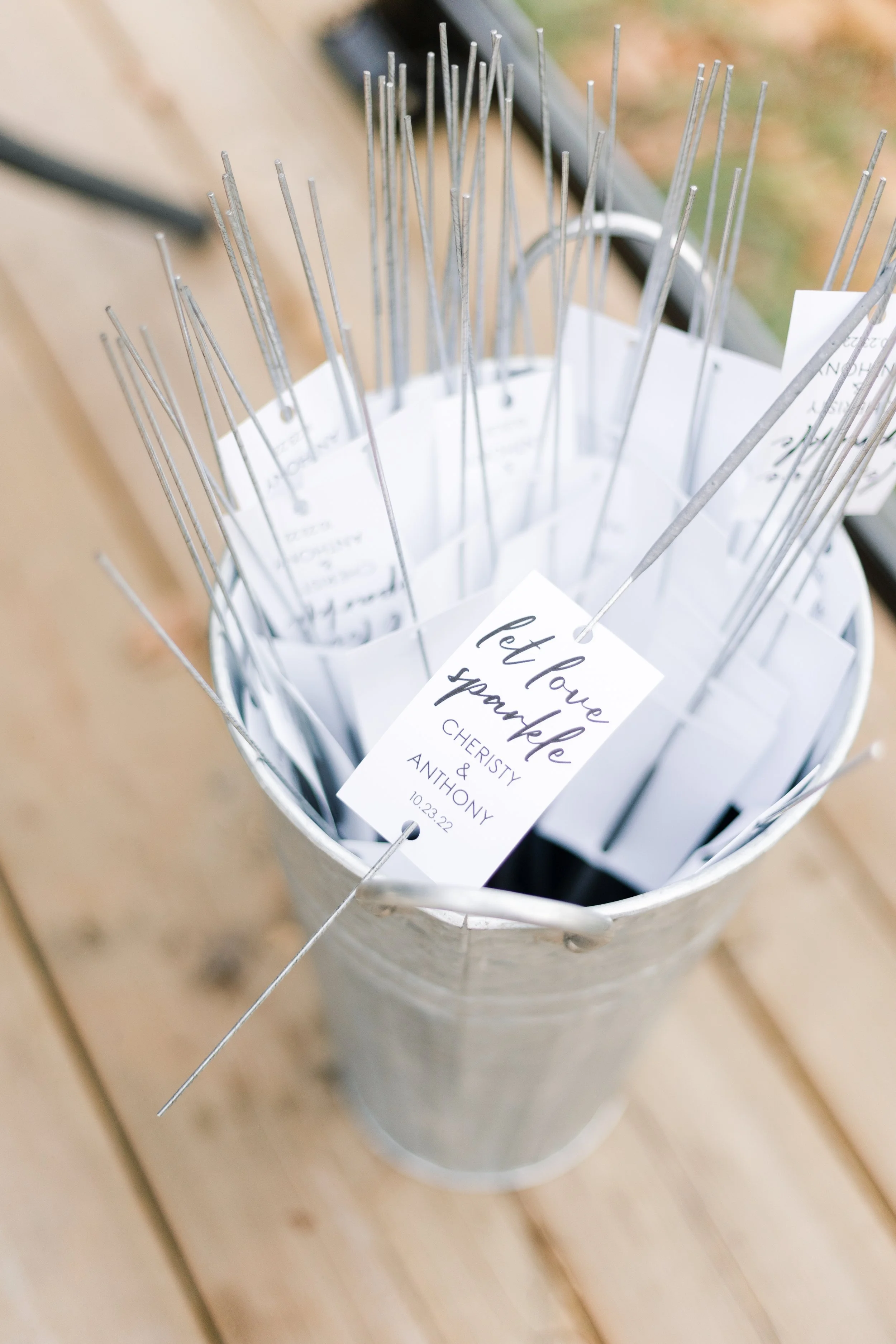 Metal container with long, thin metal picks or skewers and a wedding or event card reading "Let love sparkle, Cheristy & Anthony, 10.23.22".