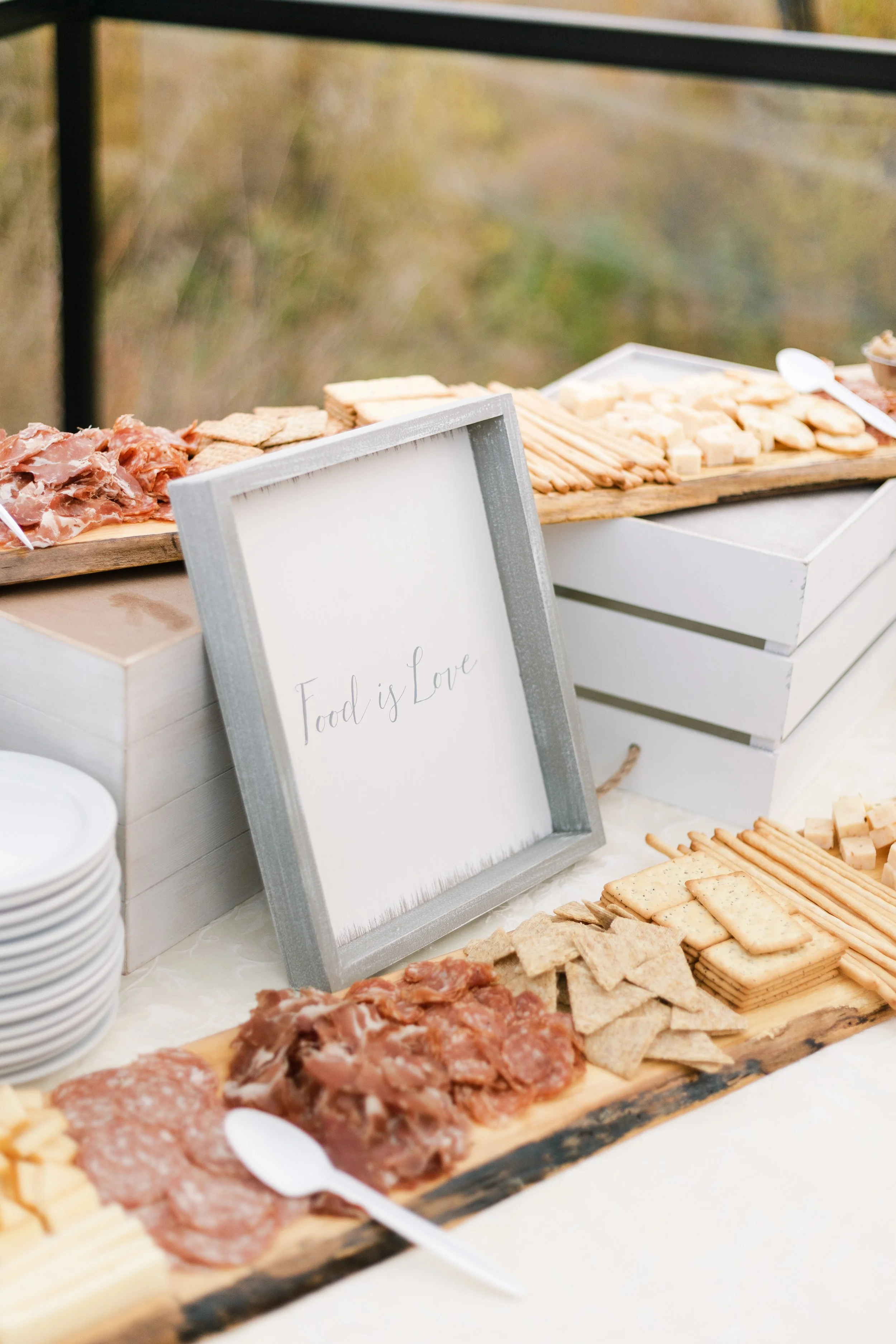 Assorted cheeses, sliced meats, and crackers arranged on a wooden serving board at a food display or buffet.