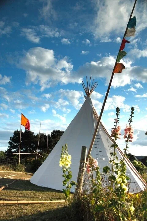 White tent set up outdoors with colorful flags and flowers, under a partly cloudy sky.
