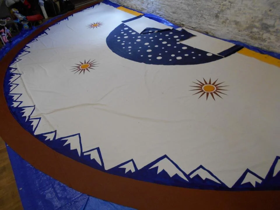 A circular fabric banner with mountain and sun designs, likely for a celebration or event, lying on a table.