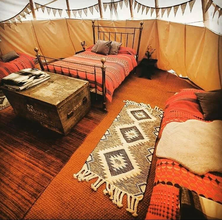 Indoor tent with a bed, a wooden chest, a rug, and a sofa with pillows, decorated with bunting flags.