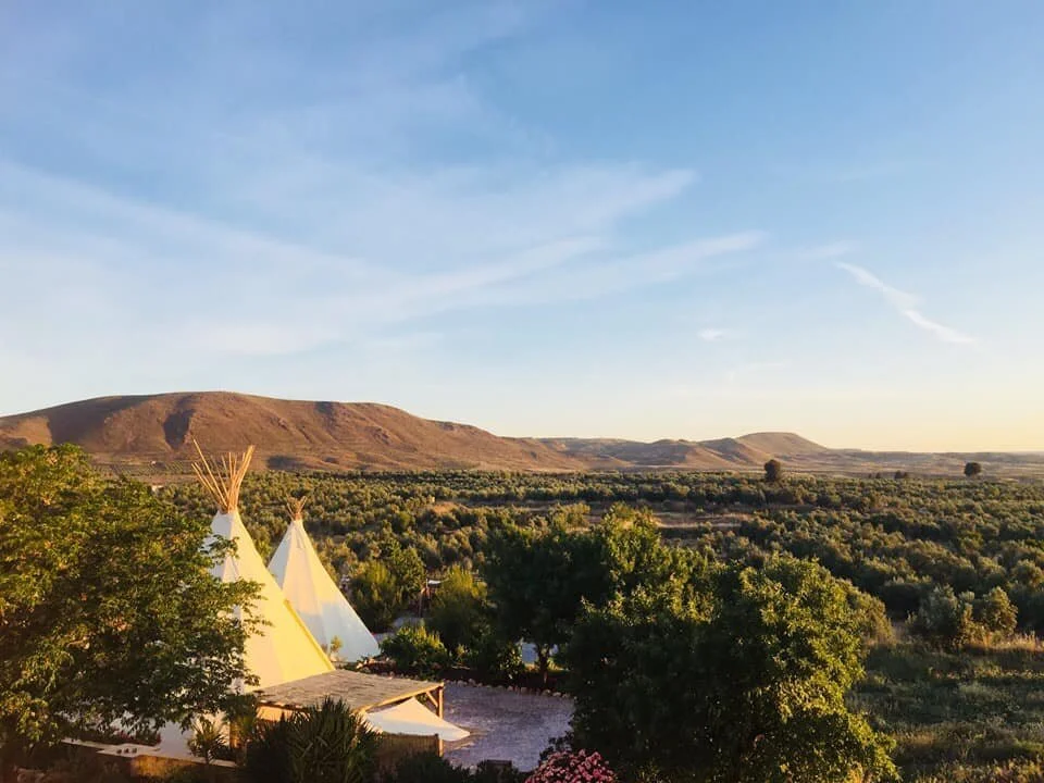 Tepees in a green landscape with mountains in the background and a blue sky with light clouds.