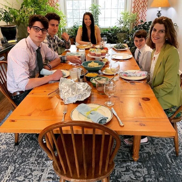 A family sitting at a wooden dining table with various dishes, smiling and posing for the photo in a bright, decorated dining room.