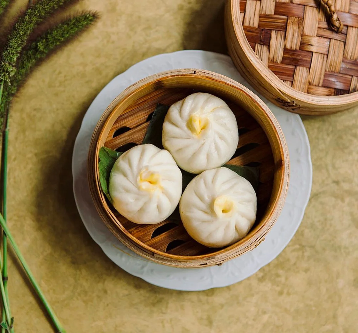 Three steamed Chinese buns in a bamboo steamer basket on a white plate.