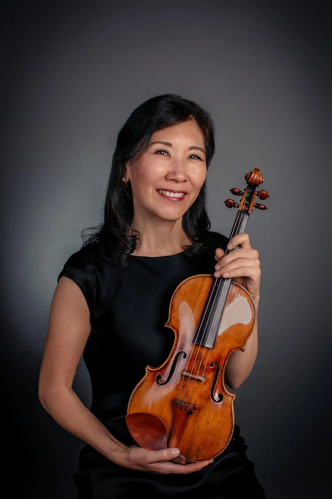 Woman holding a violin and smiling, indoors with natural light.