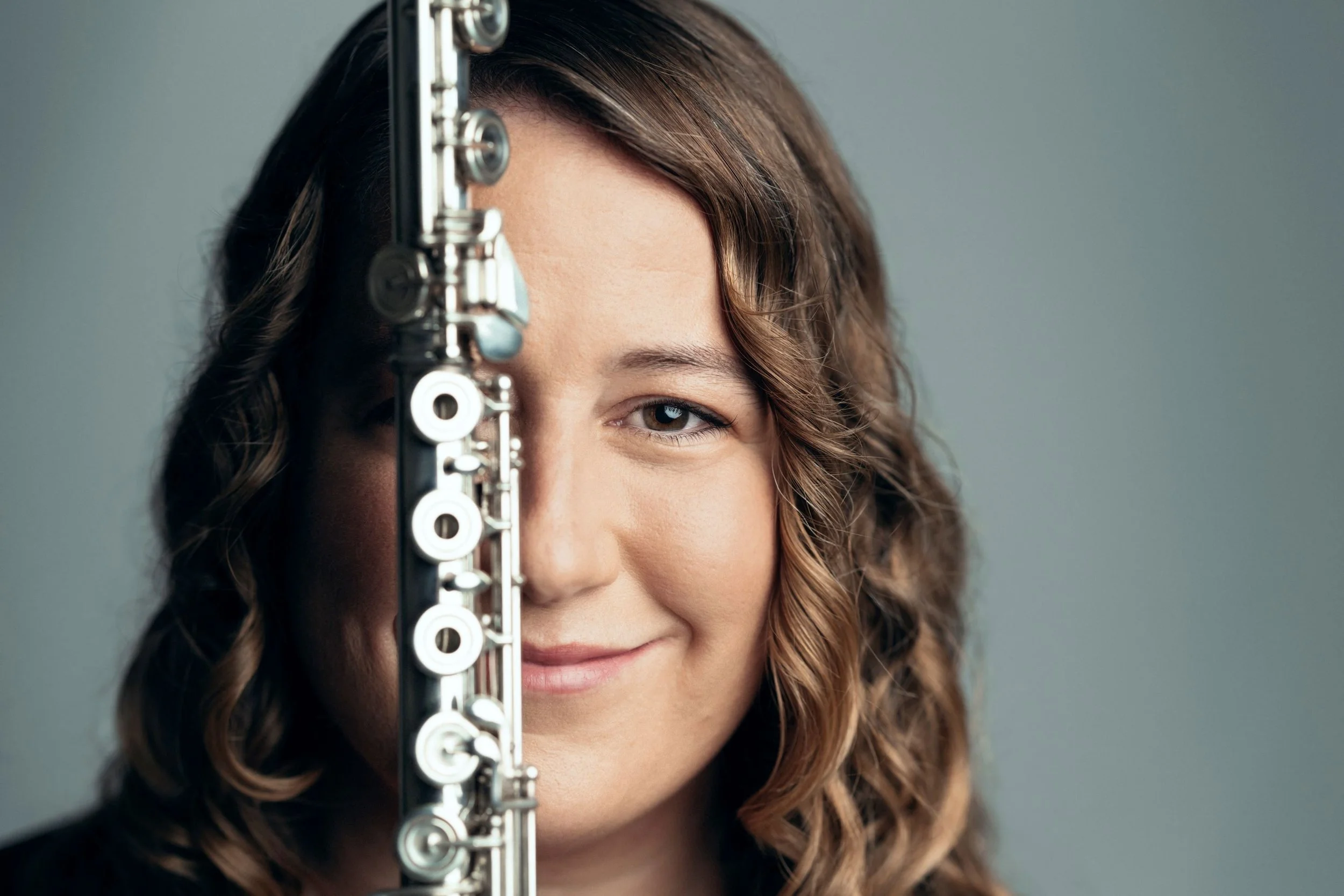 Black and white photo of a woman with long curly hair, holding a flute, standing outdoors in front of a blurred background.