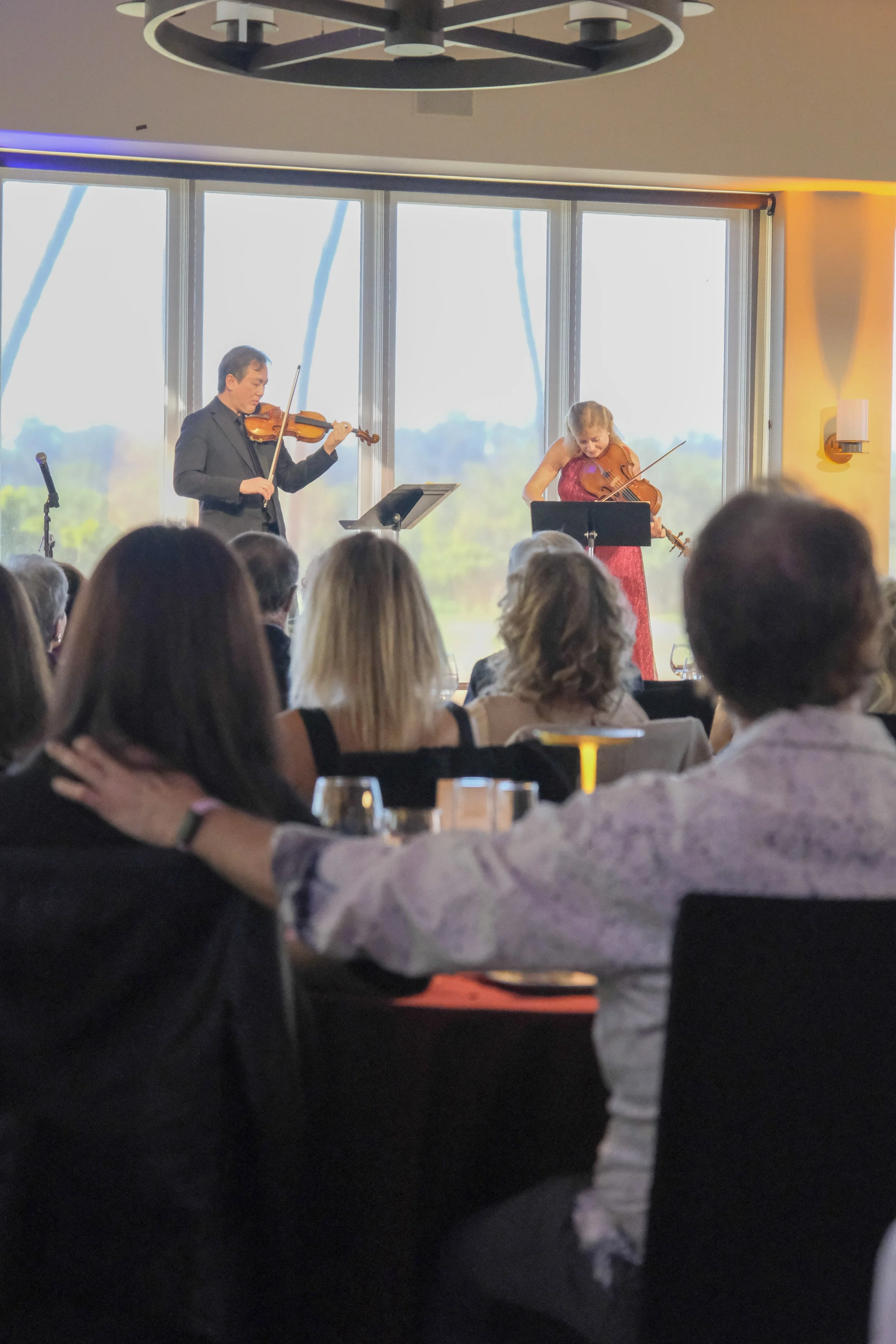 Orchestra musicians performing on stage, with string instruments and music stands.