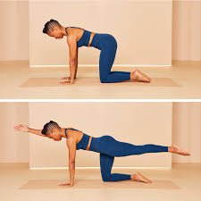 Woman in blue workout clothes doing a bird-dog in a warmly lit yoga studio.