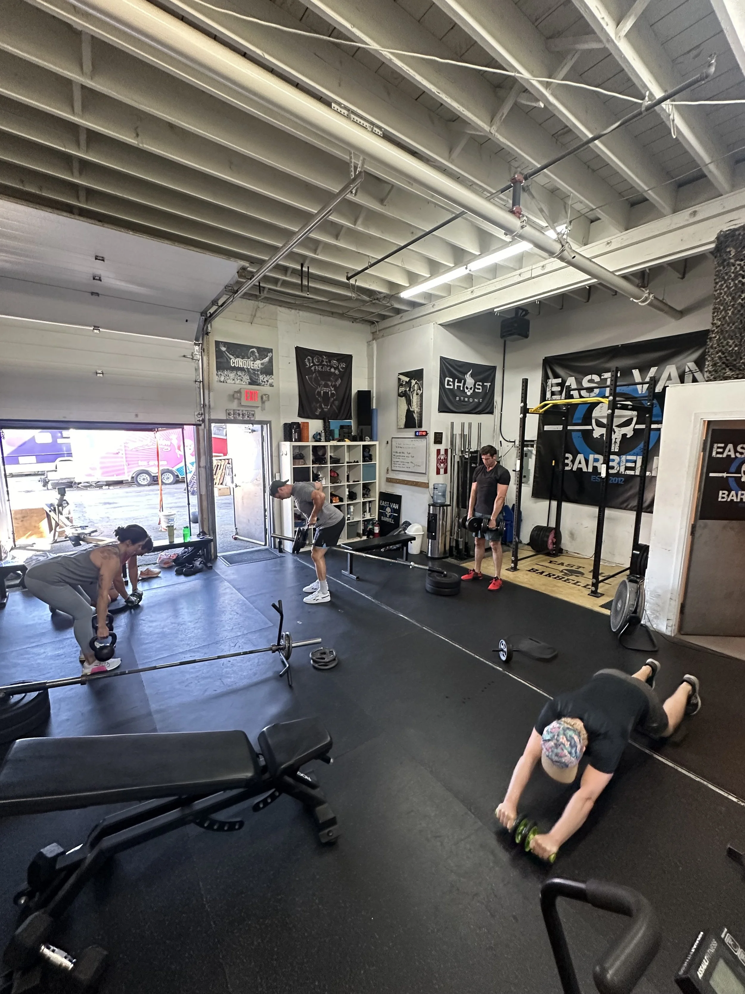 People working out in a gym, lifting weights and using exercise equipment, with banners on the walls.