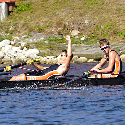 Two people in a kayak on a river, one raising a fist in celebration, both wearing sunglasses and life jackets.