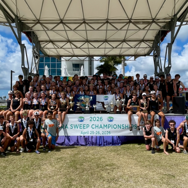 A large group of young athletes on a stage at an outdoor sports event, celebrating their championship win in 2026, with trophies and medals displayed, on April 25-26, 2026.