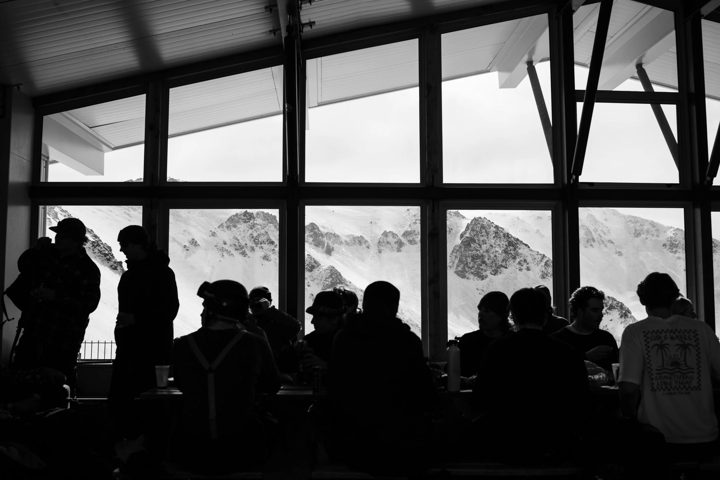 Silhouettes of people inside a building with large windows revealing snow-covered mountains outside.