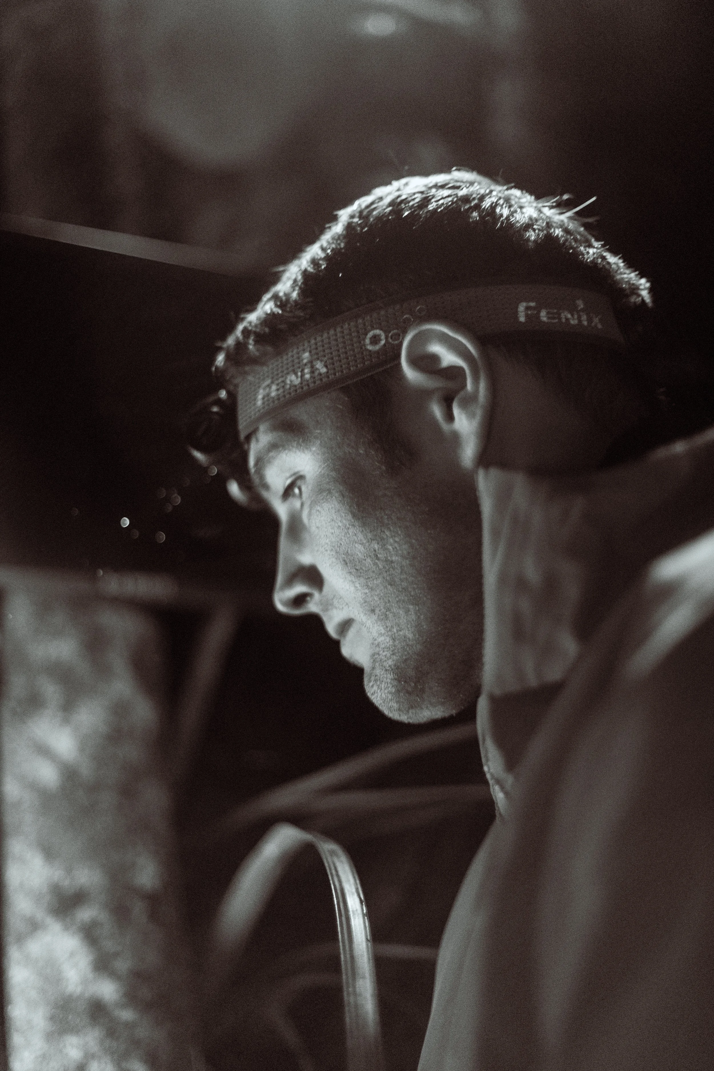A black and white close-up of a man's profile, wearing safety goggles labeled 'FENIX', with short hair and focused expression.