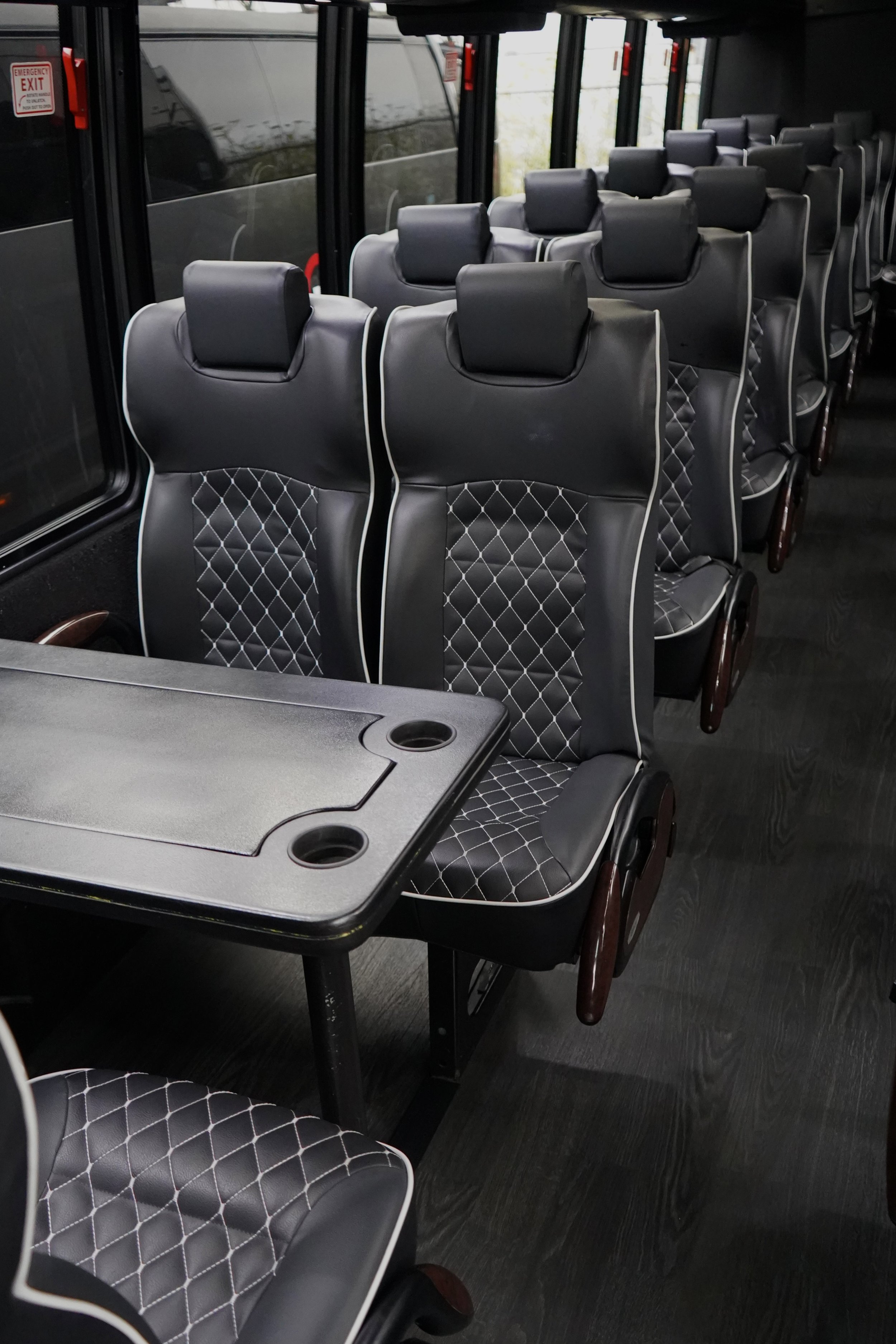 Interior of a bus with black leather seats featuring diamond stitching, and a black table with cup holders.