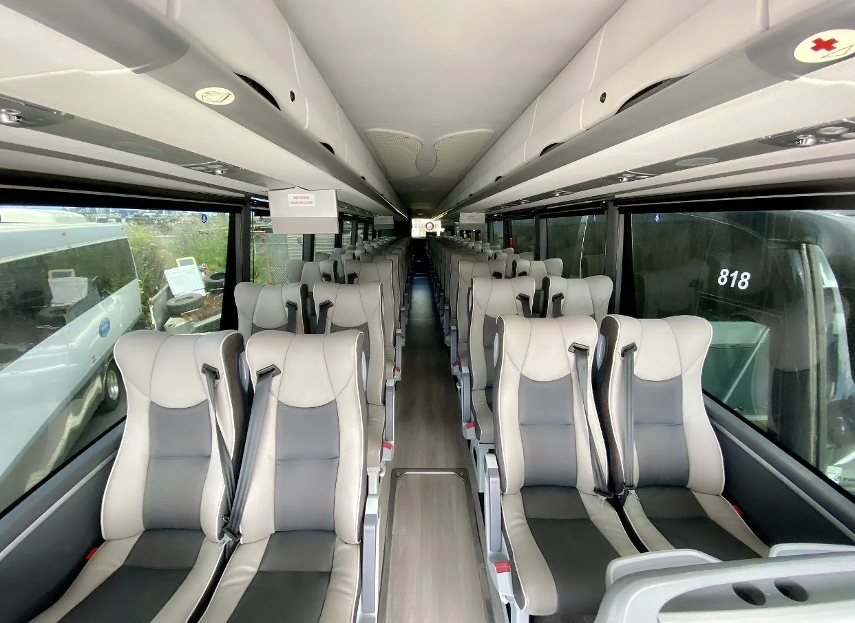 Interior of a modern coach bus with beige and gray seats, large windows, and overhead storage.