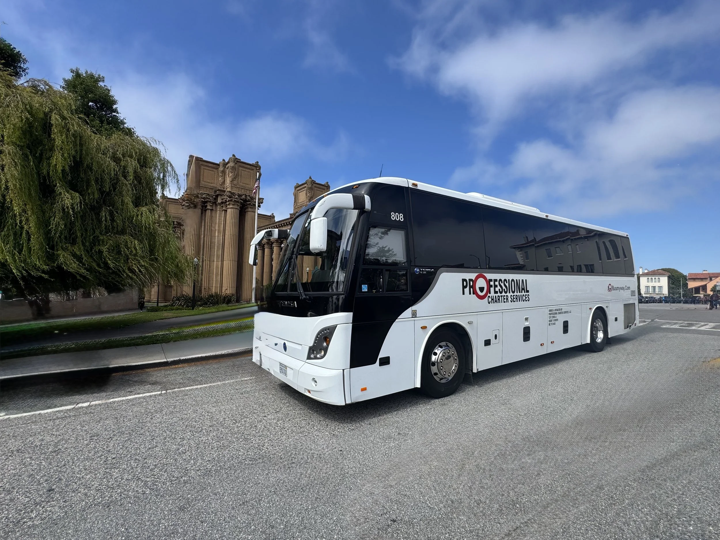 A black and white bus with the words "Professional Charter Services" parked on a city street near a historic building with columns and trees, under a partly cloudy sky.