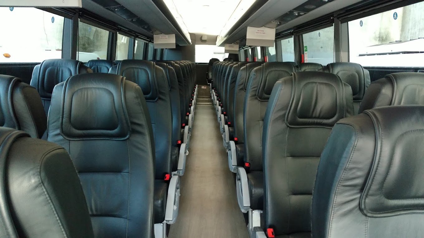 Interior of an empty tour bus with rows of black leather seats and windows on both sides.