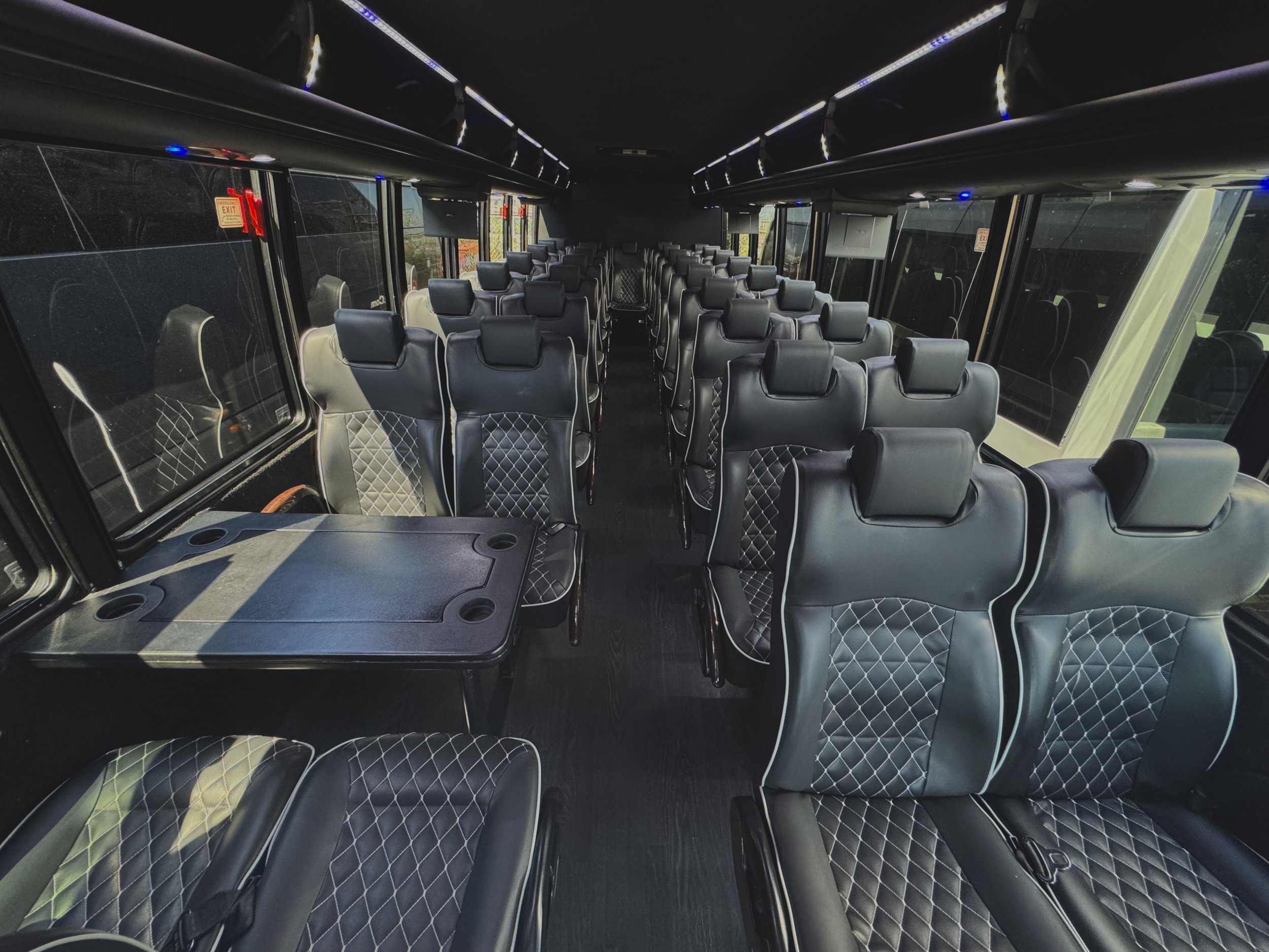 Interior of a bus with black leather seats, window seats available, and a small table at the front.