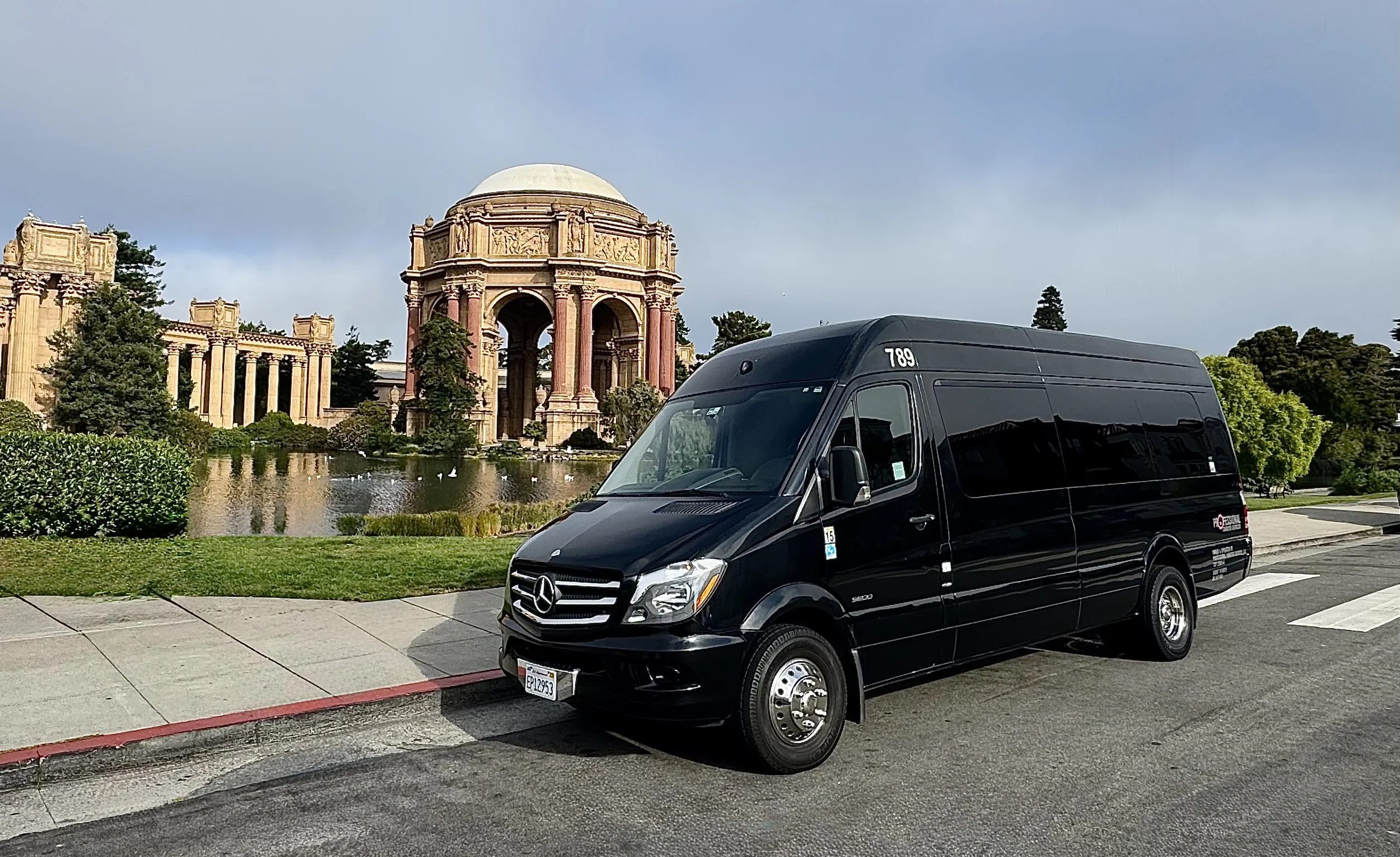 Black Mercedes-Benz Sprinter van parked on the street in front of a historic building with columns, a pond, and trees.