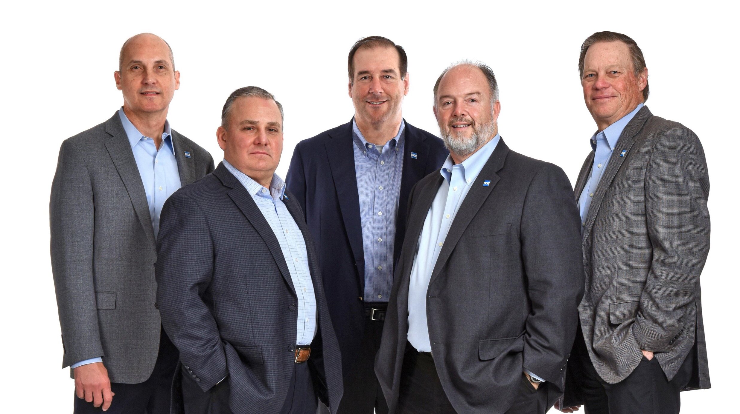 Group of five men in suits posing against a white background