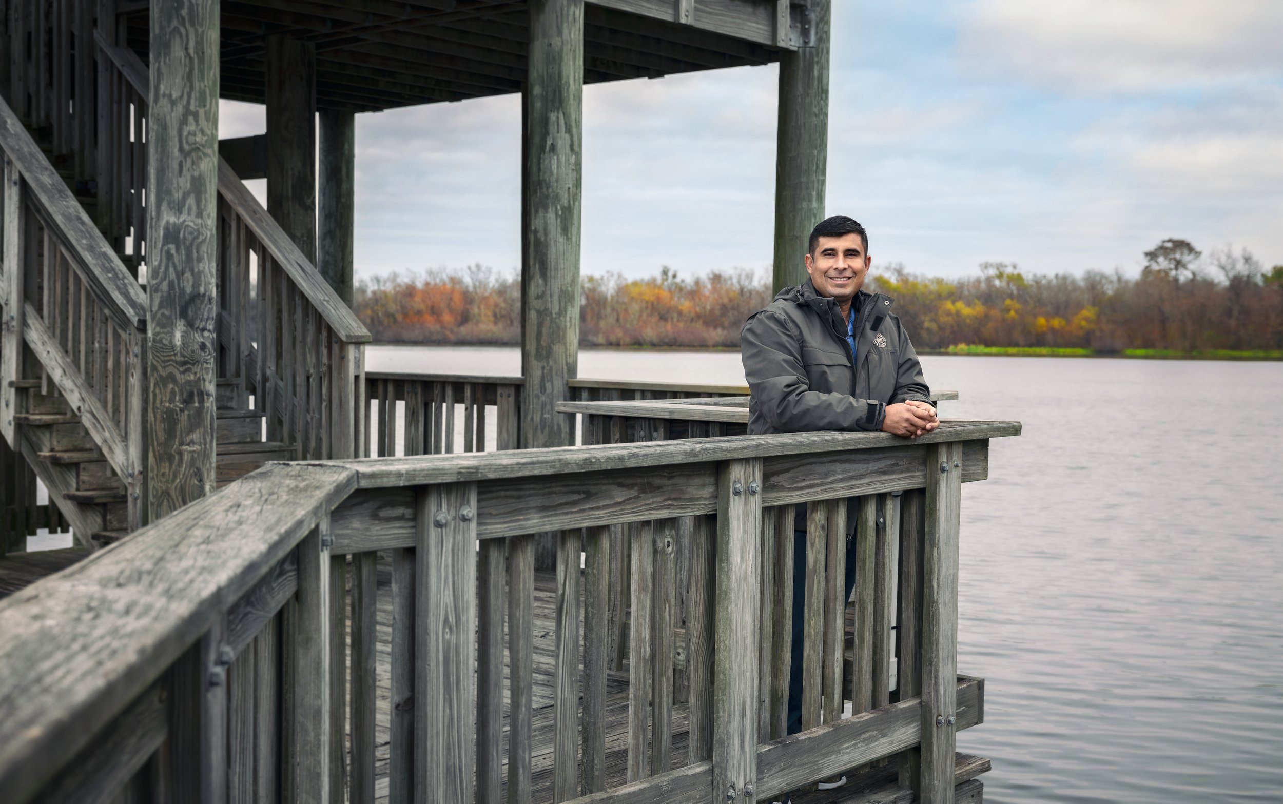 Person standing on a wooden dock overlooking a lake with autumn trees in the background.