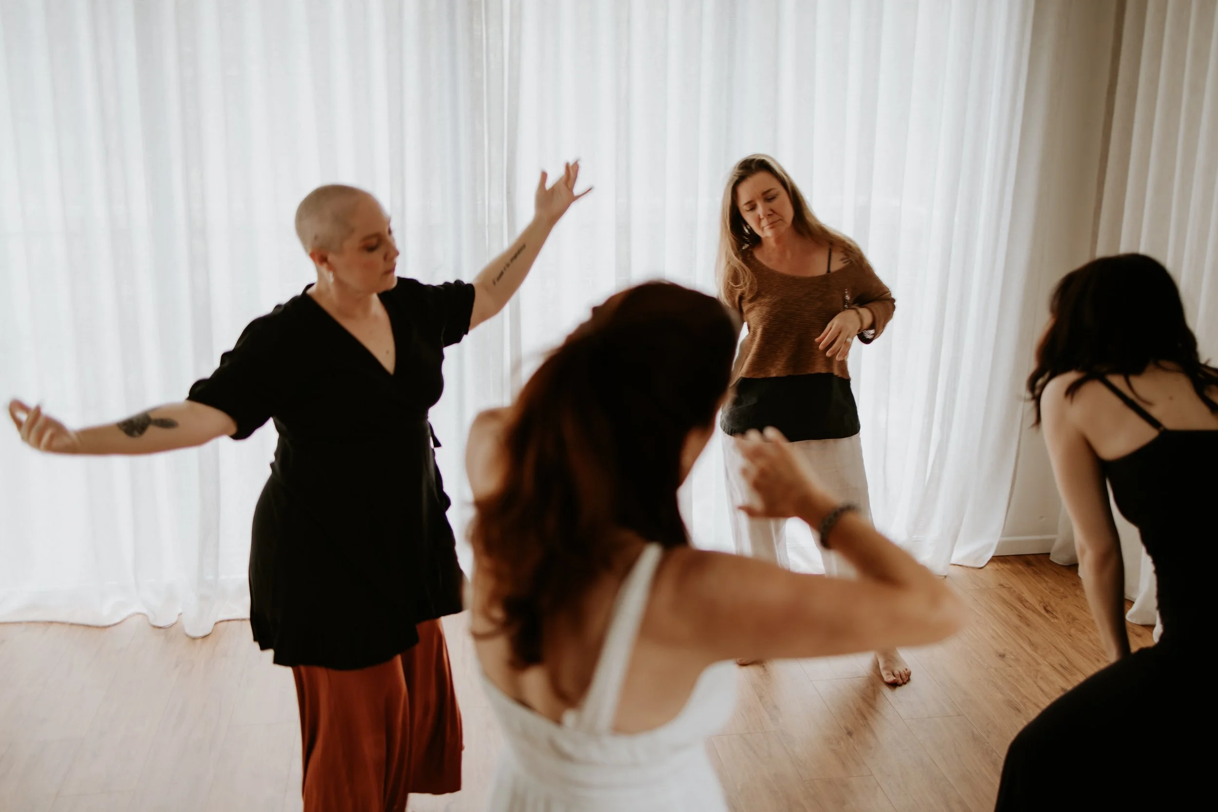 Group of women participating in a yoga or meditation class in a bright room with sheer curtains.