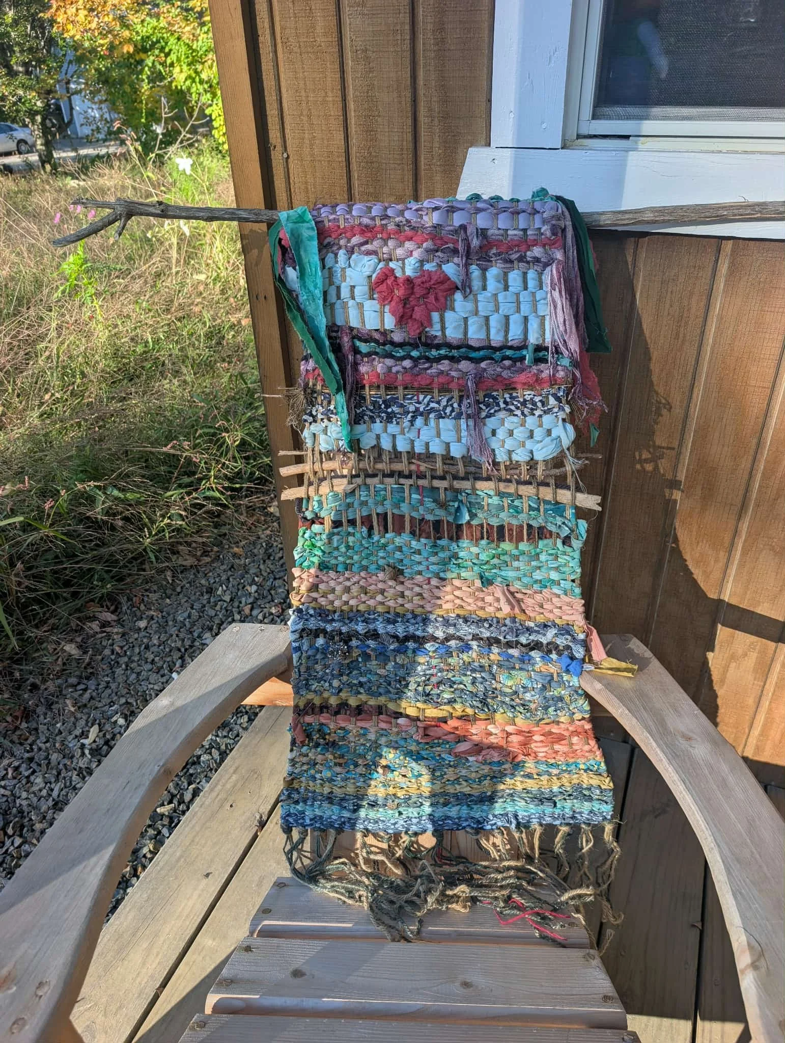 Colorful woven rag rug hanging on a wooden chair outdoors next to a house wall.