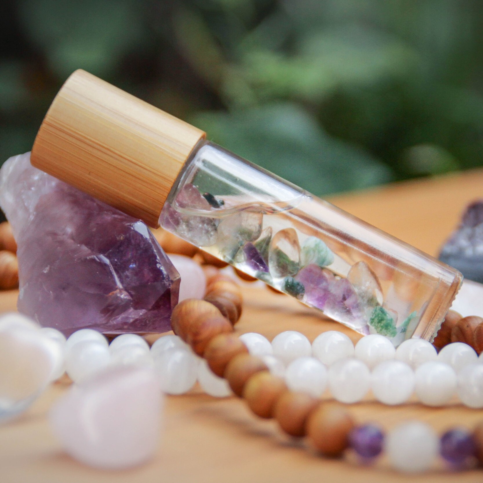 Close-up of a glass vial with a bamboo cap, filled with colorful crystals, placed on purple stones and surrounded by round beads.