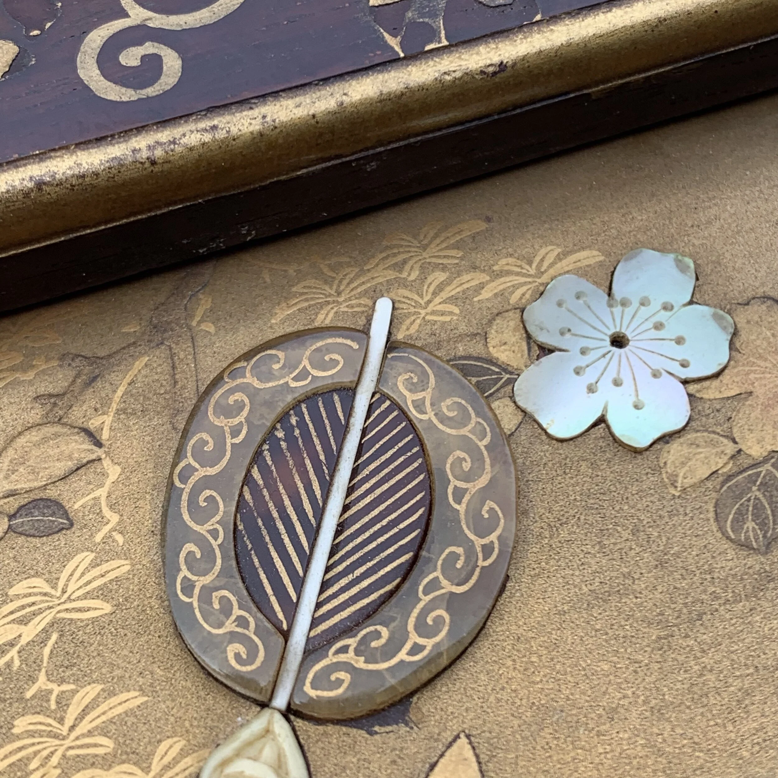 Close-up of a decorative item featuring a circular arrow-shaped element and a white flower with a metallic outline on a gold and brown patterned surface.