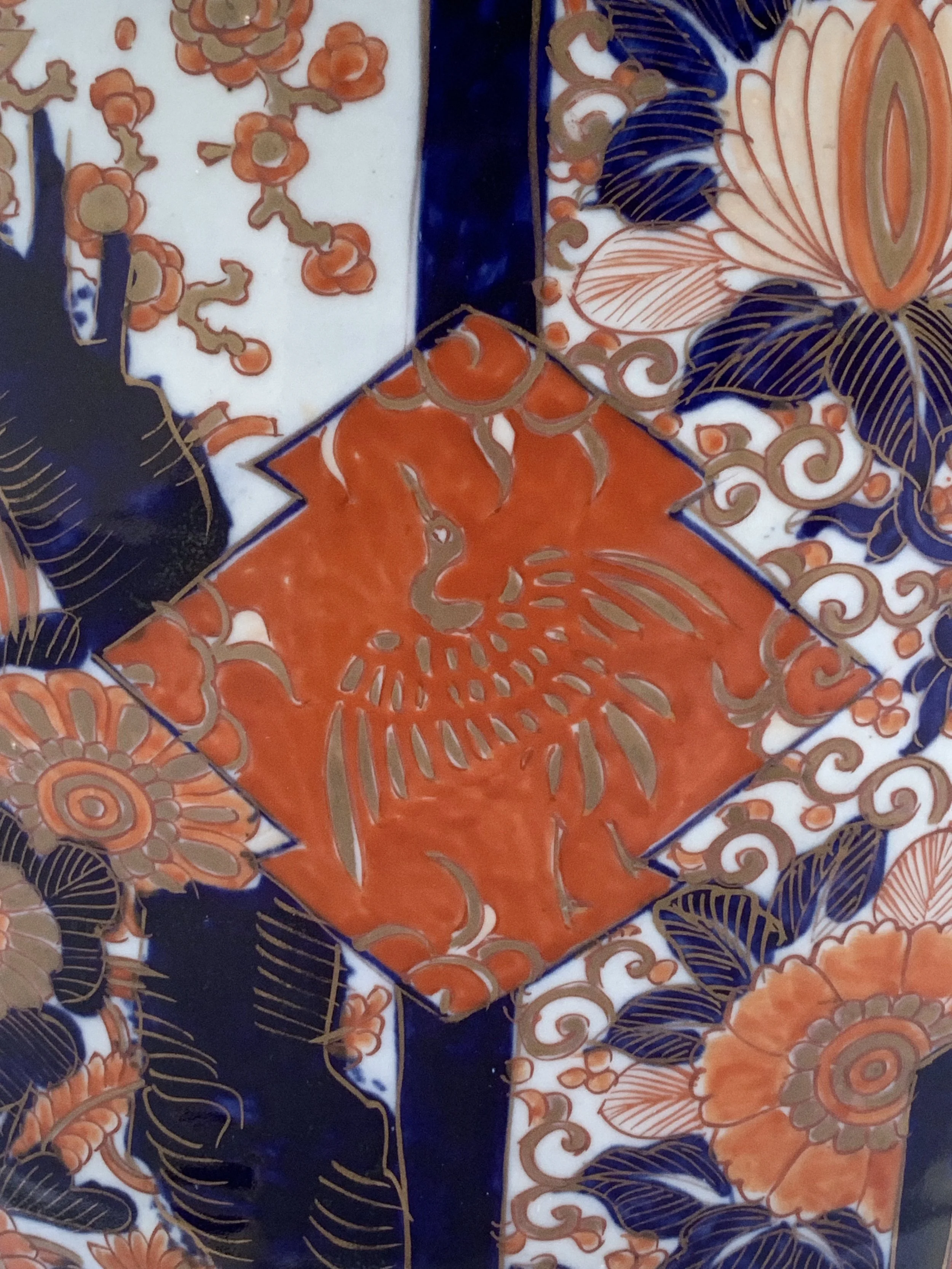 Decorative ceramic tile with floral patterns, featuring a central orange flower, navy blue leaves, and intricate gold lines.