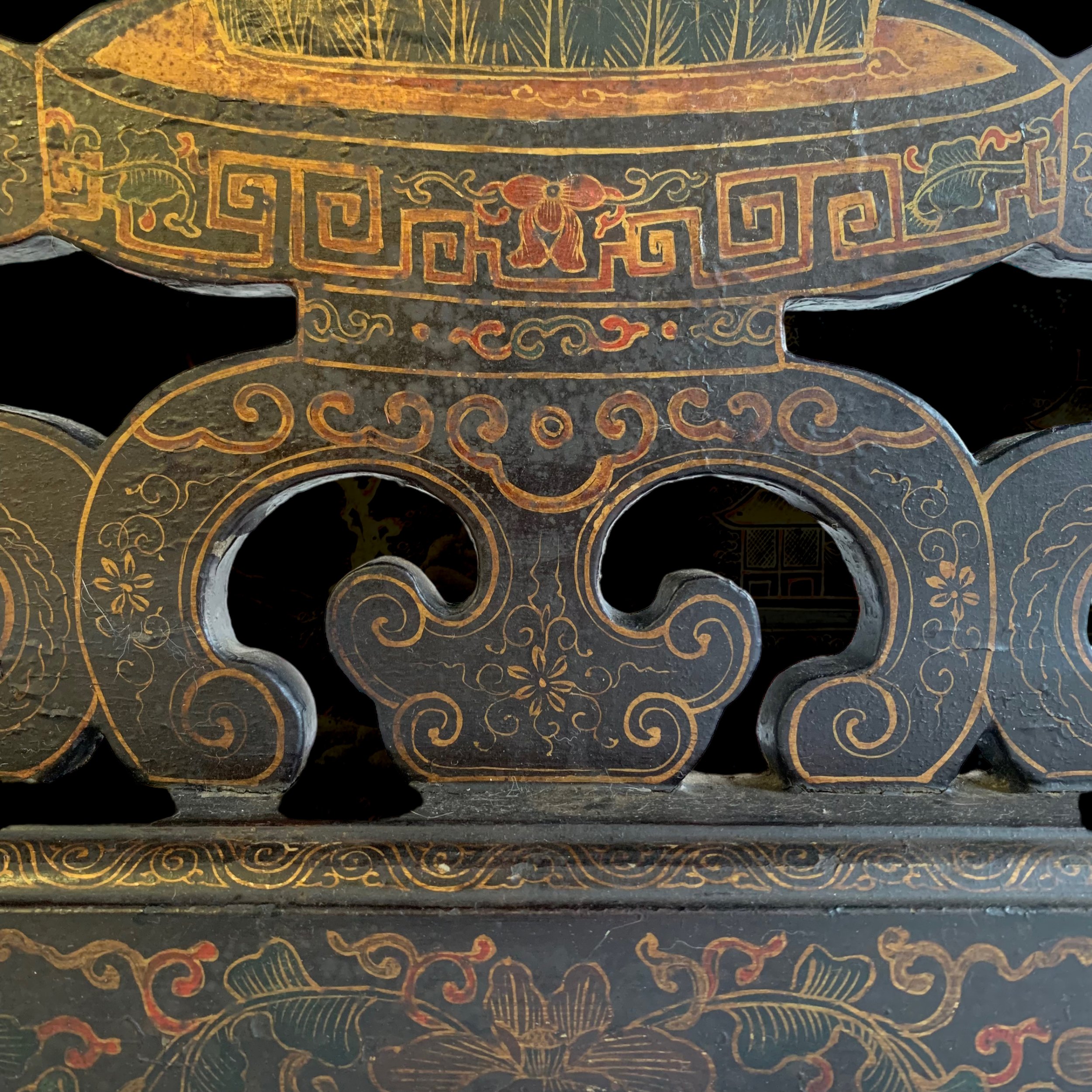 Close-up of ornately decorated black wooden surface with gold and red intricate floral and geometric patterns.