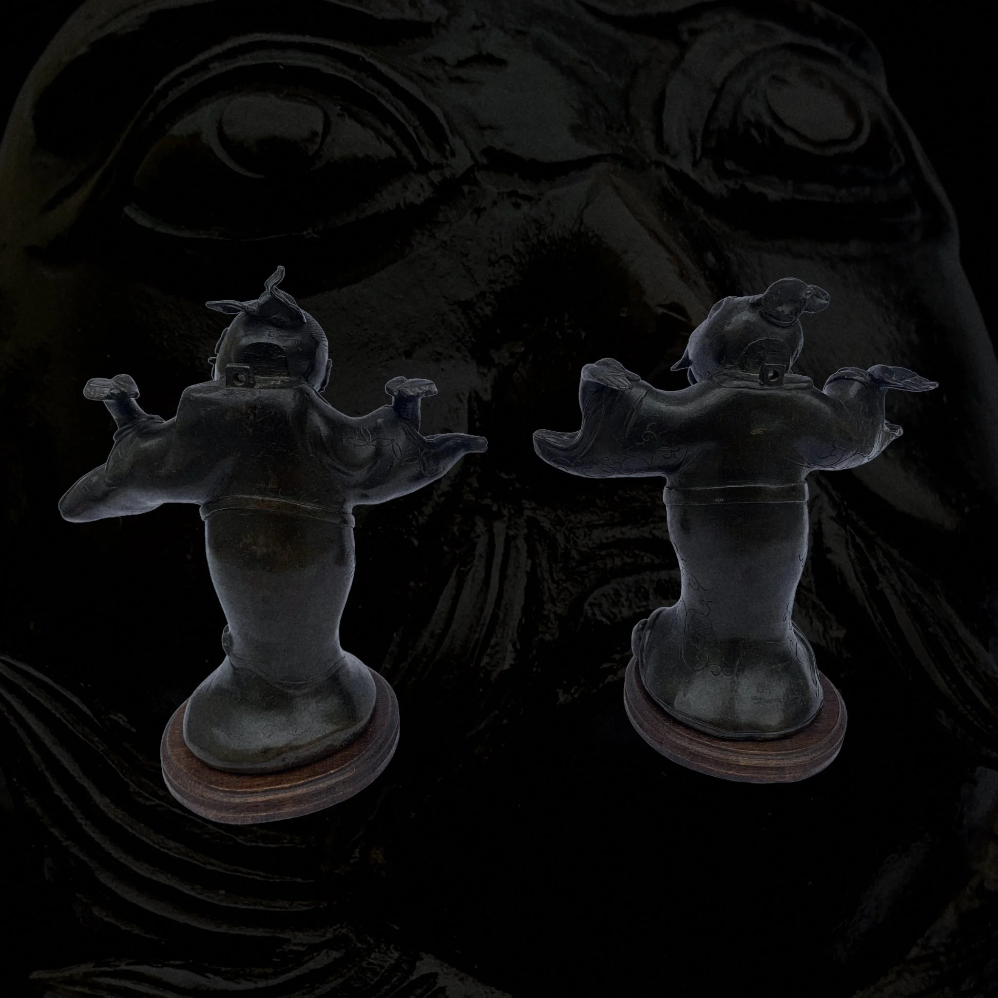 Two black decorative sculptures of Chinese guardian lions mounted on wooden bases, with each lion's mouth open and detailed features, set against a dark background with a faint image of a face.