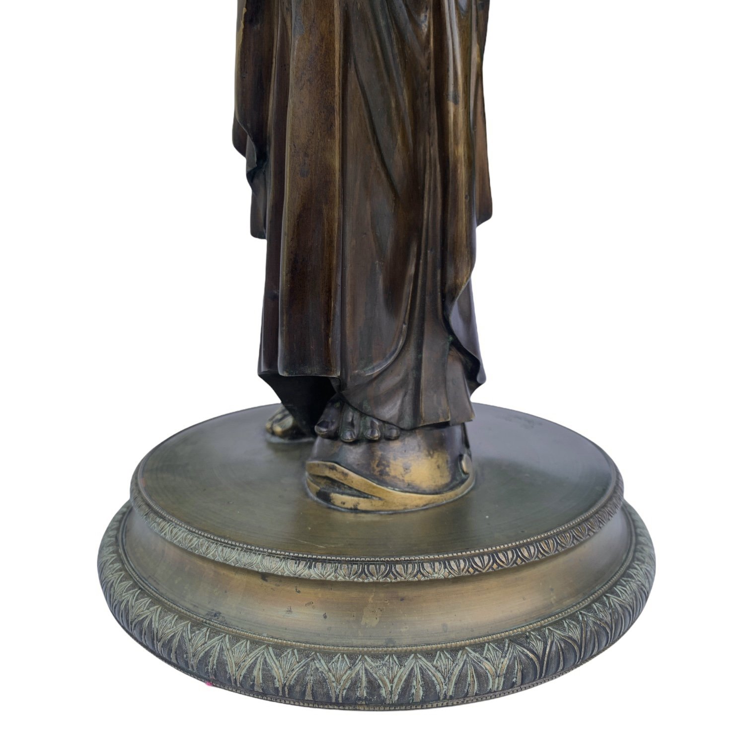 Close-up of the lower part of a bronze statue depicting a person barefoot, standing on a decorative circular base.