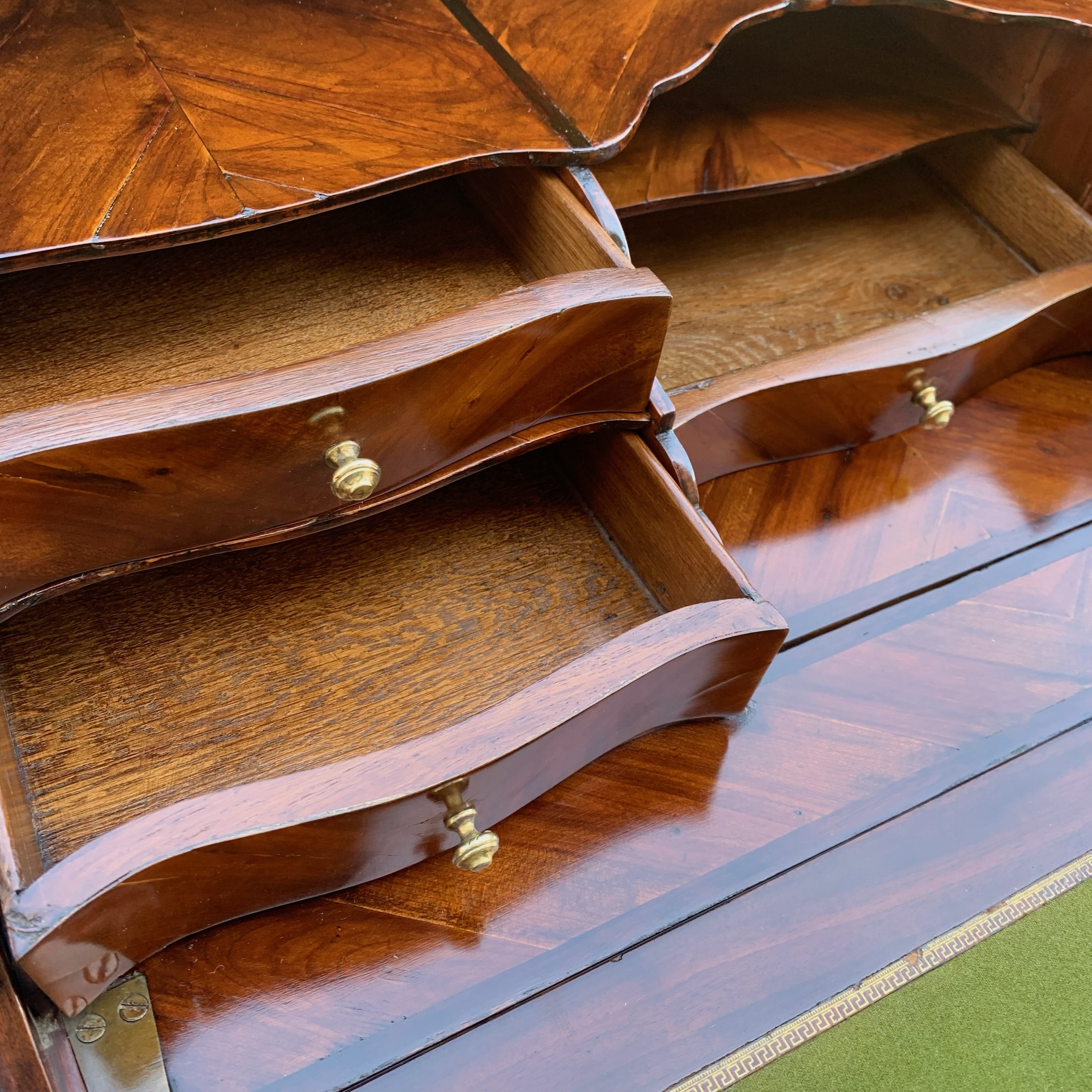 Close-up of a wooden drawer chest with open drawers and small brass knobs, placed on a dark polished wooden surface.