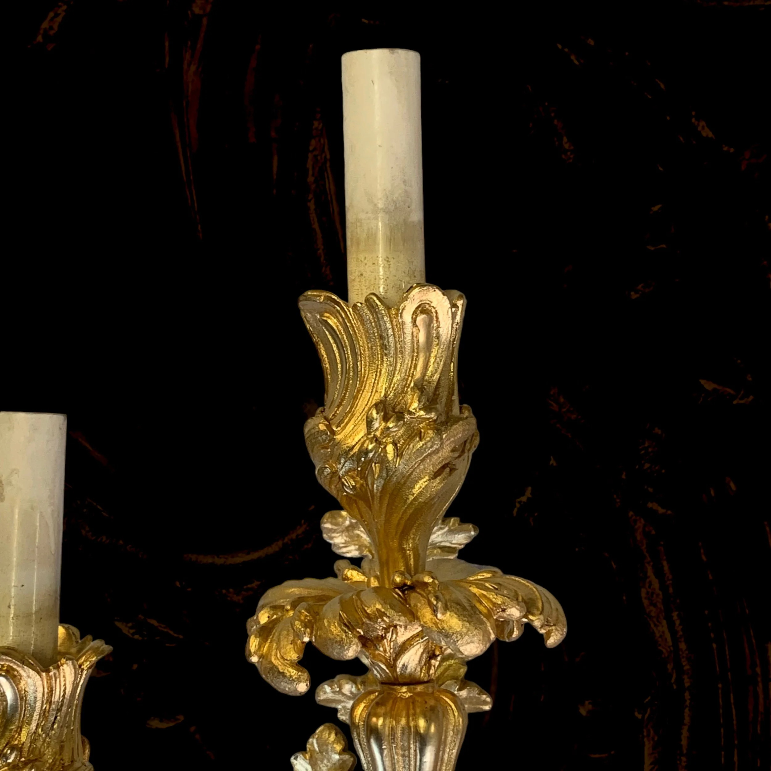 Close-up of a gold-colored ornate wall sconce with an unlit candle against a dark background.