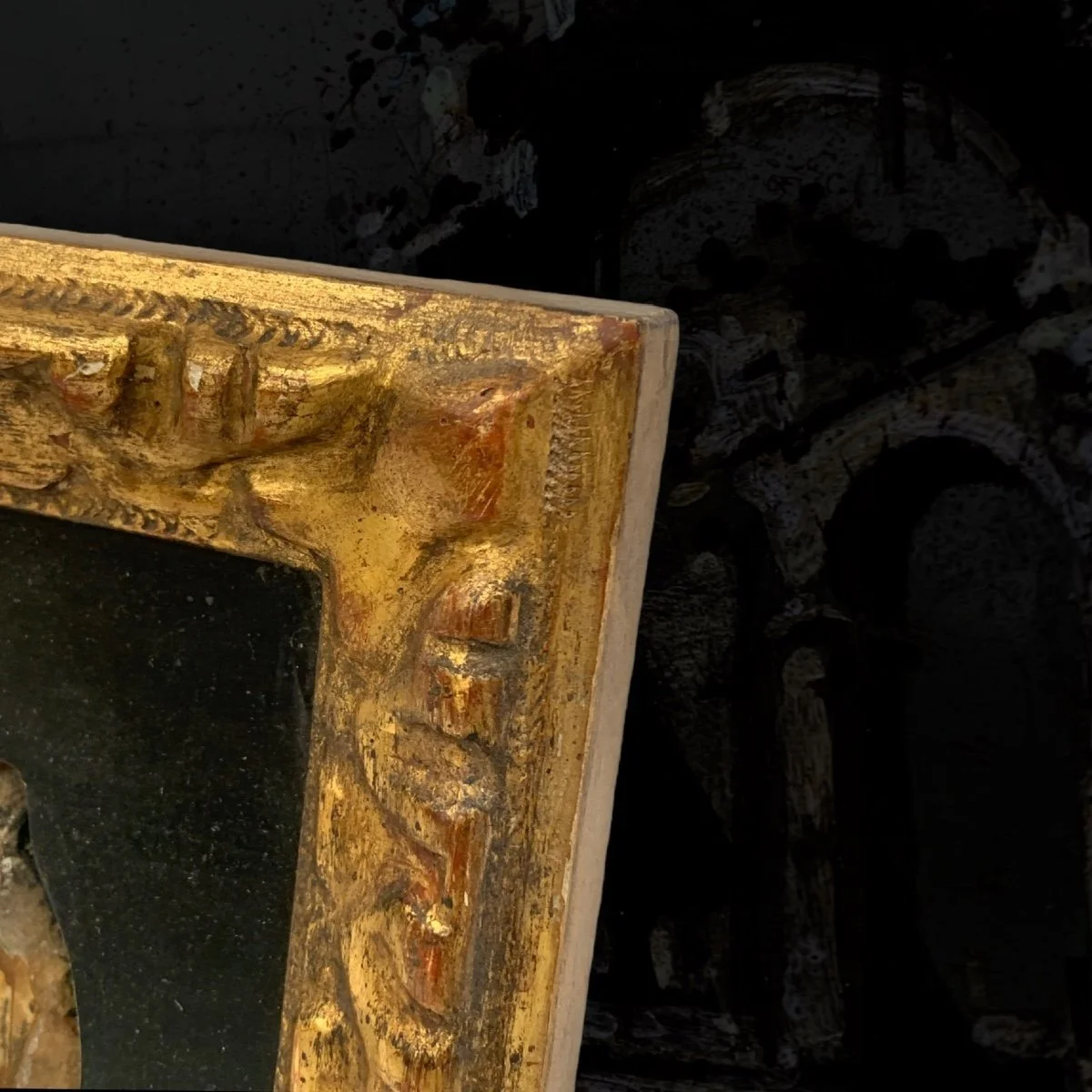 Close-up of an ornate gold-trimmed frame with a black background, possibly a painting or mirror, with intricate detailing and some visible wear.