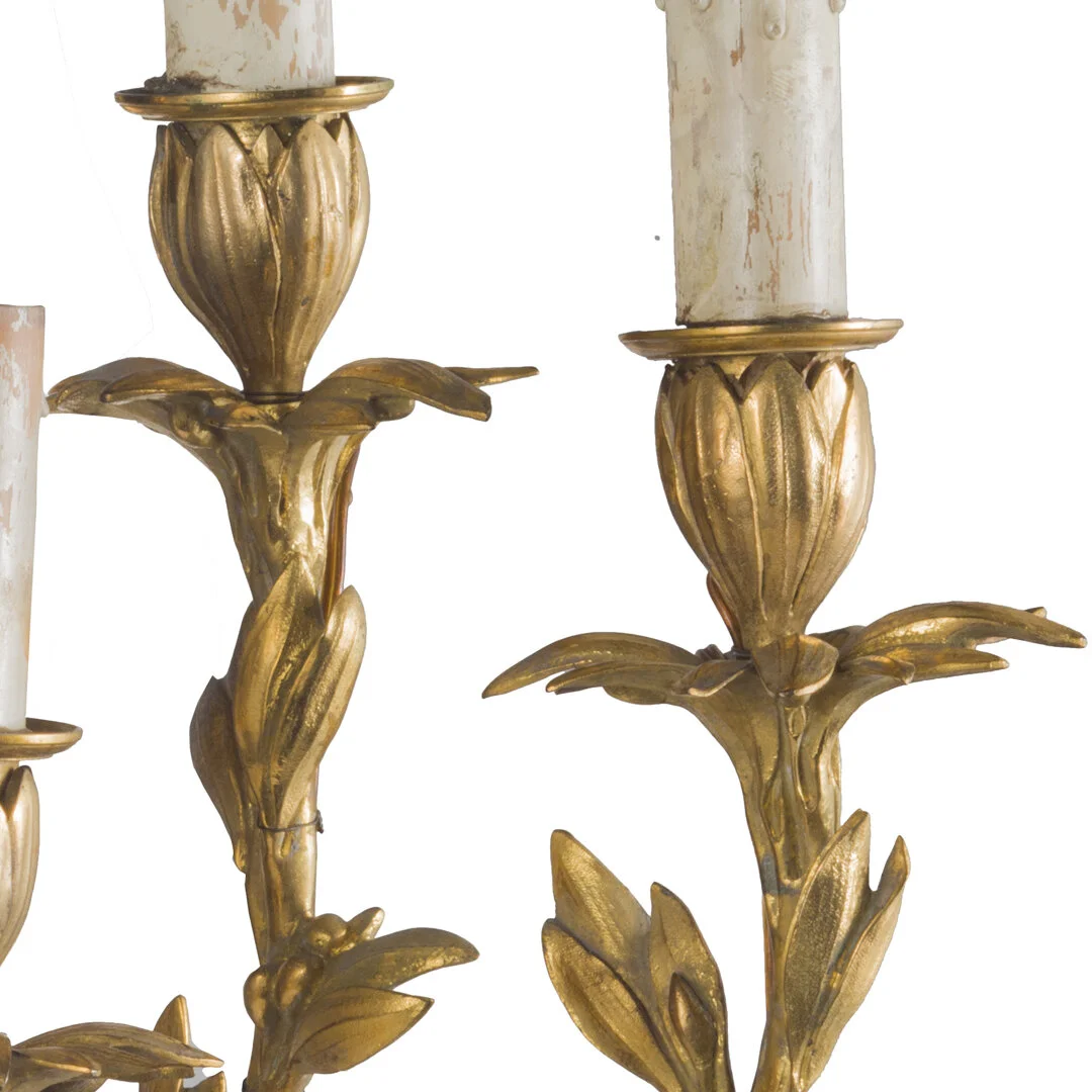 Close-up of a vintage gold-colored wall sconce with candle holders and decorative floral motifs.